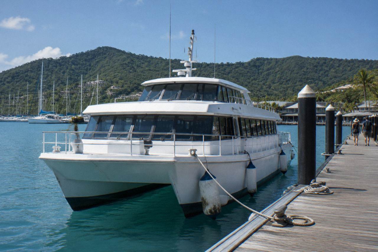A passenger ferry moored at a tropical marina jetty beside calm blue water