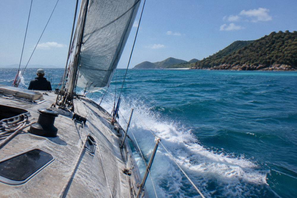 A maxi yacht heeling under full sail in open water between green islands
