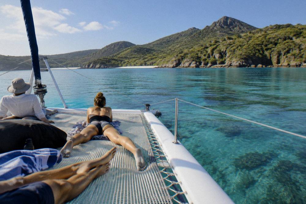 A group of passengers relaxing on the wide deck of a catamaran at anchor