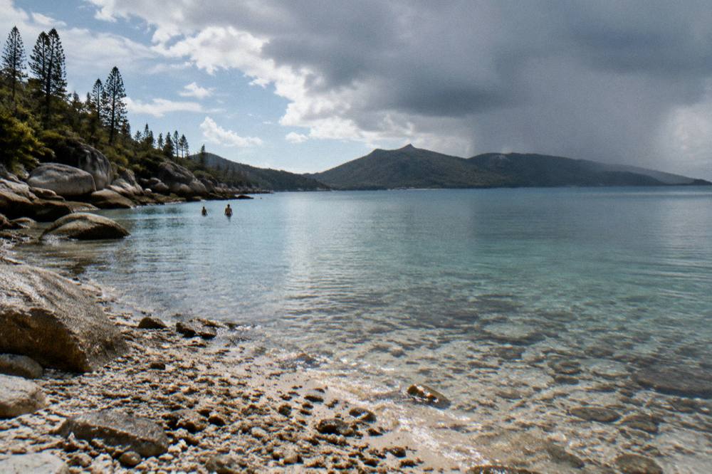 A calm morning sea with a distant rain shower over islands and clearing sky above