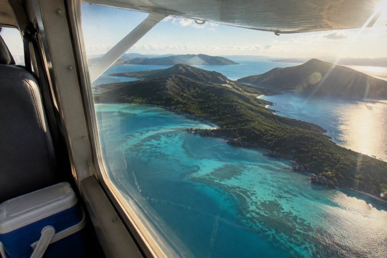 A light aircraft banking over turquoise reef water and green islands on a clear day