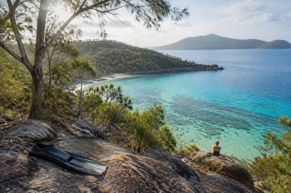 A wooded tropical island shoreline with reef water shading from pale green to deep blue