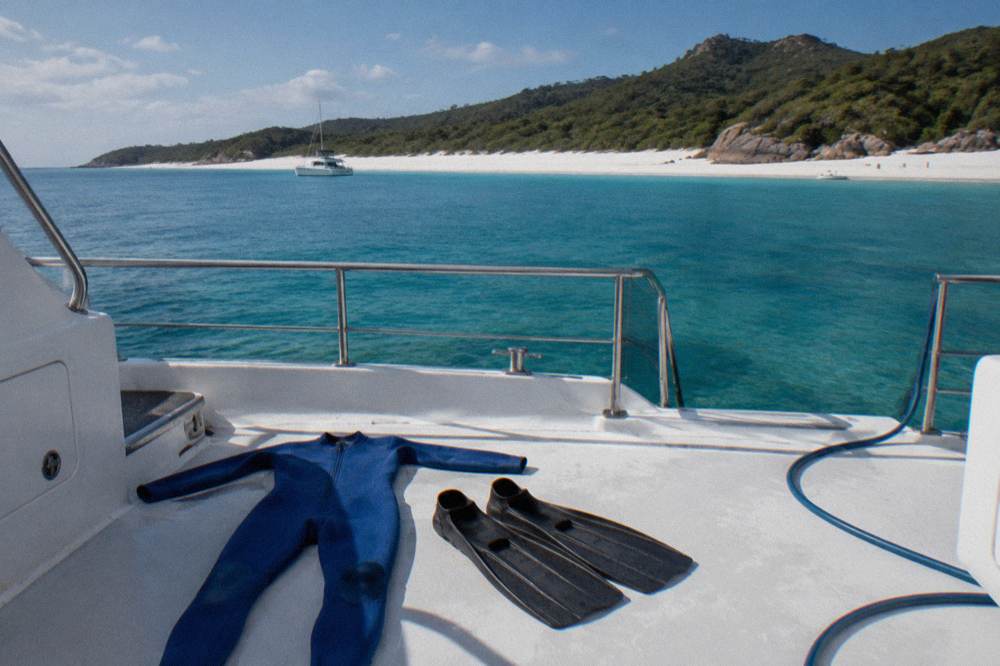 A full-length lycra stinger suit laid out on a boat deck beside snorkel fins