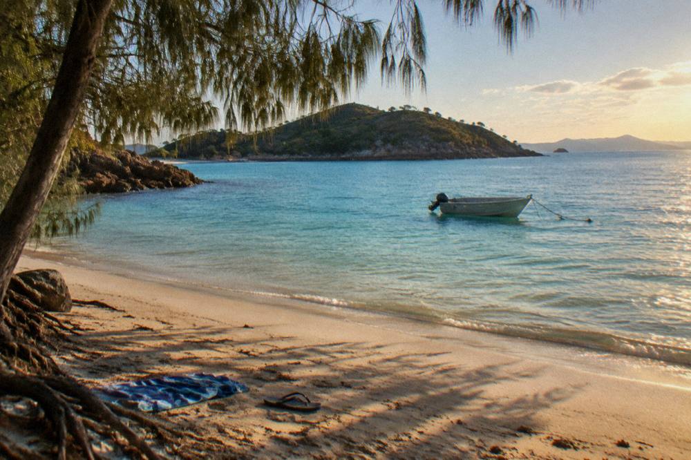 A small anchored boat over pale reef water near an island beach