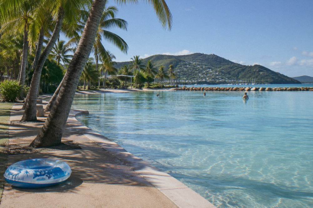 A large sheltered swimming lagoon beside a palm-lined foreshore in a tropical town