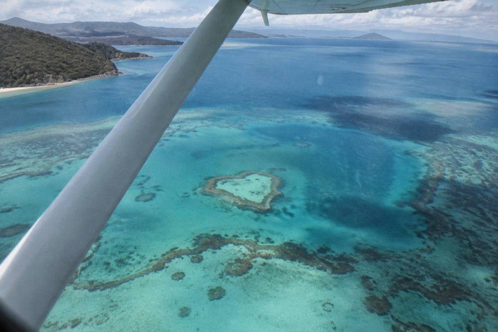 A light aircraft banking over a heart-shaped coral reef in turquoise sea